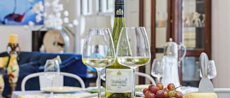 A dining table with a bottle of wine, glasses, grapes, and cheese.
