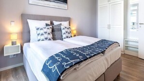 A neatly made bed with a blue and white patterned blanket, a grey headboard, and a wall-mounted abstract painting. - 4 Star Holiday Home in Travemunde (Lübeck)