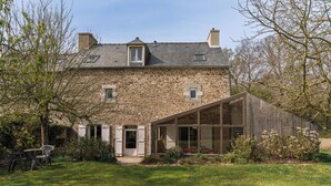 A stone house with a large glass extension, a wooden deck, and a grassy yard.