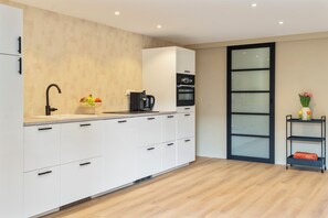 A modern kitchen with white cabinets, a black faucet, a fruit bowl, a coffee machine, and a built-in oven. - Casa Florita - Cozy apartment in Noordwijkerhout. (Noordwijkerhout)