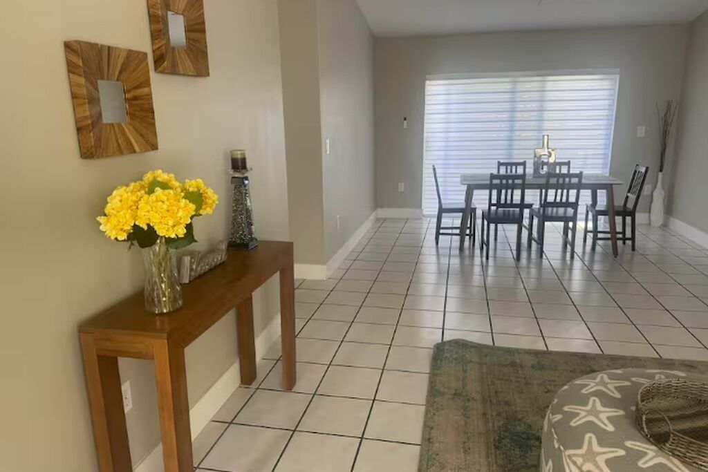 Uma área de refeições com uma mesa e cadeiras, um aparador com um vaso de flores e um tapete estampado.