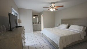 A bedroom with a bed, a ceiling fan, a television on a wooden dresser, and a bathroom visible in the background. - Miami Retreat with Backyard Pool (Miami)
