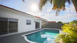 A residential swimming pool with a white house, a garage, and a wooden fence. - Miami Retreat with Backyard Pool (Miami)