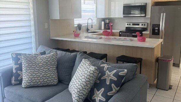 A modern kitchen with a central island, stainless steel appliances, and a grey sofa with patterned cushions. - Miami Retreat with Backyard Pool (Miami)