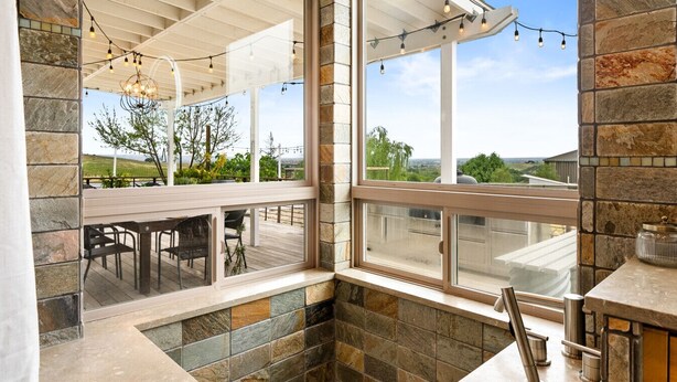 A stone-walled bathroom with a large window, a wooden bench, and a tiled floor.