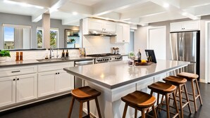 A modern kitchen with white cabinetry, a large island with stools, stainless steel appliances, and a view of the outdoors.