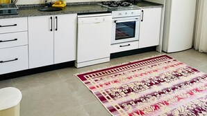 A kitchen with white cabinets, a stove, an oven, a refrigerator, and a patterned rug. - Fethiye  Merkezde Harika Ev (Fethiye)