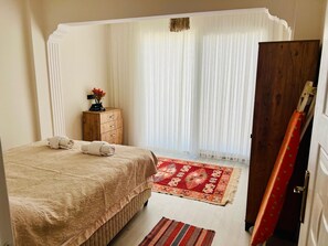 Une chambre à coucher avec un lit, une commode en bois, un tapis rouge à motifs et une porte avec un rideau rouge.