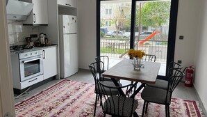 A modern kitchen with white cabinets, a gas stove, and a refrigerator. There is a dining table with chairs and a vase of flowers. - Fethiye  Merkezde Harika Ev (Fethiye)