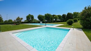 En rektangulär swimmingpool med en kakelbeklädd poolkant, omgiven av välskött gräsmatta och träd.