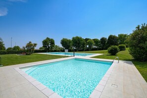 Ein rechteckiger Swimmingpool mit Fliesen umgeben, mit einer gepflegten Rasenfläche und Bäumen.