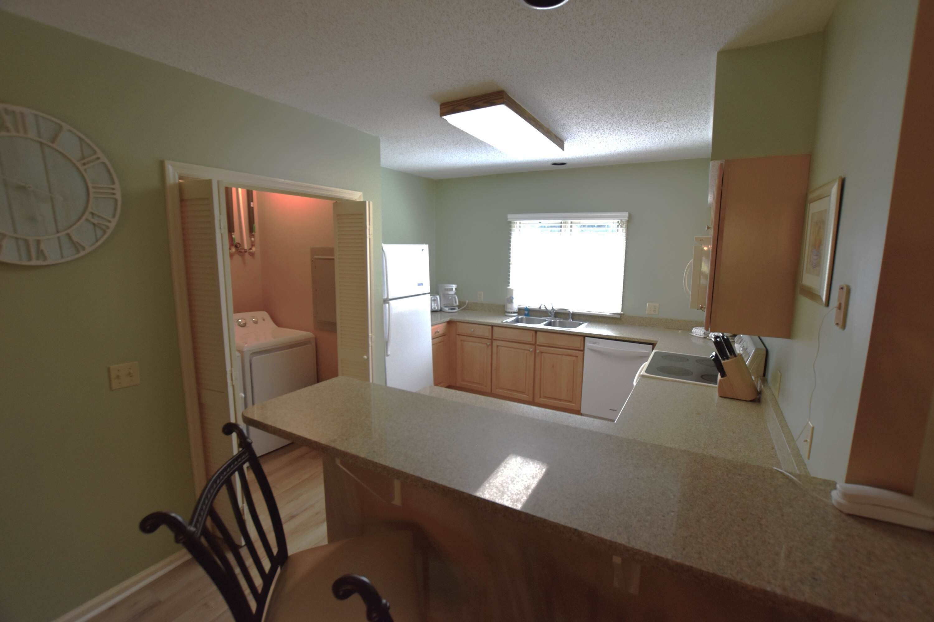 A kitchen with wooden cabinets, a built-in oven, a sink, and a clock on the wall.