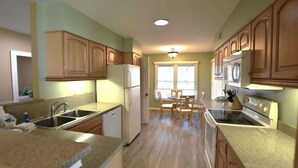 A kitchen with wooden cabinets, a refrigerator, an oven, and a dining area with a table and chairs. - Shipyard Villa, Lagoons, Golf, Pool & Beach Nearby (Hilton Head Island)