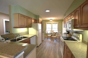 A kitchen with wooden cabinets, a refrigerator, an oven, and a dining area with a table and chairs. - Shipyard Villa, Lagoons, Golf, Pool & Beach Nearby (Hilton Head Island)