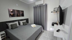 A hotel room with a bed, a flat-screen TV, a small table, and a wall-mounted TV. - Eden Residential - Apartment 10 Air Conditioning Hot/Cold (Sorocaba)