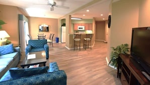 A living room with a sofa, armchair, and coffee table, a kitchen with a microwave and chairs, and a TV on a stand. - Family Hilton Head Getaway, Pool, Beach Access, Sleeps 6 (Hilton Head Island)