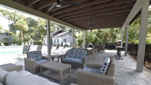 A covered outdoor seating area with wicker furniture, a pool, and a house in the background. - Family Hilton Head Getaway, Pool, Beach Access, Sleeps 6 (Hilton Head Island)