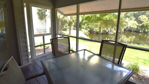 Eine überdachte Terrasse mit Tisch und Stühlen, großen Fenstern und Blick auf einen Teich und viel Grün.