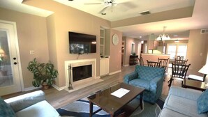 A living room with a fireplace, sofas, a coffee table, a TV, and a dining area with chairs. - Shipyard Escape, Beach Access, Pool, Golf & Lagoon Views (Hilton Head Island)