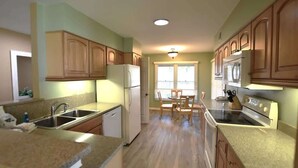 A kitchen with wooden cabinets, a refrigerator, stove, and a dining area with a table and chairs. - Shipyard Escape, Beach Access, Pool, Golf & Lagoon Views (Hilton Head Island)