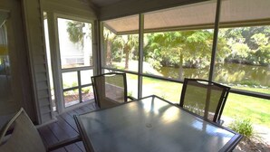 A covered patio with a table and chairs, large windows with a view of a pond and greenery. - Shipyard Escape, Beach Access, Pool, Golf & Lagoon Views (Hilton Head Island)