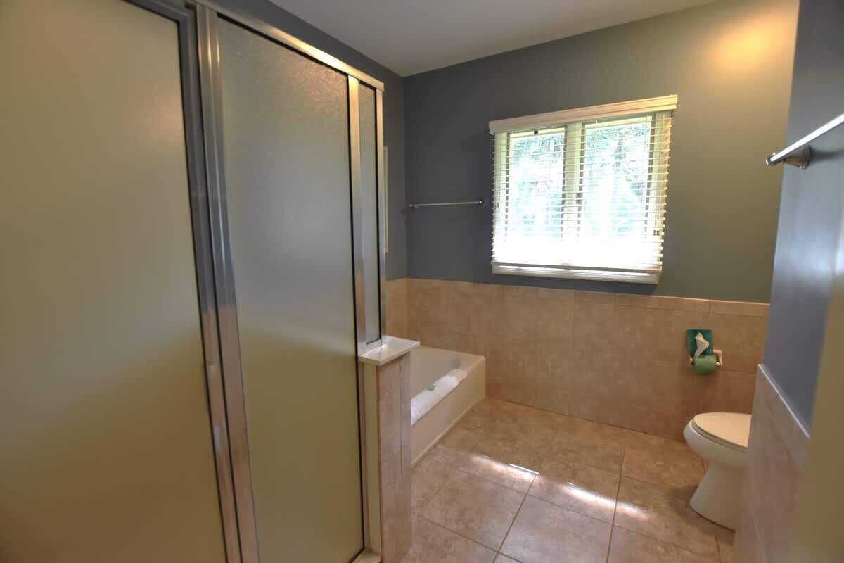 A bathroom with a shower, bathtub, toilet, and a window with blinds.