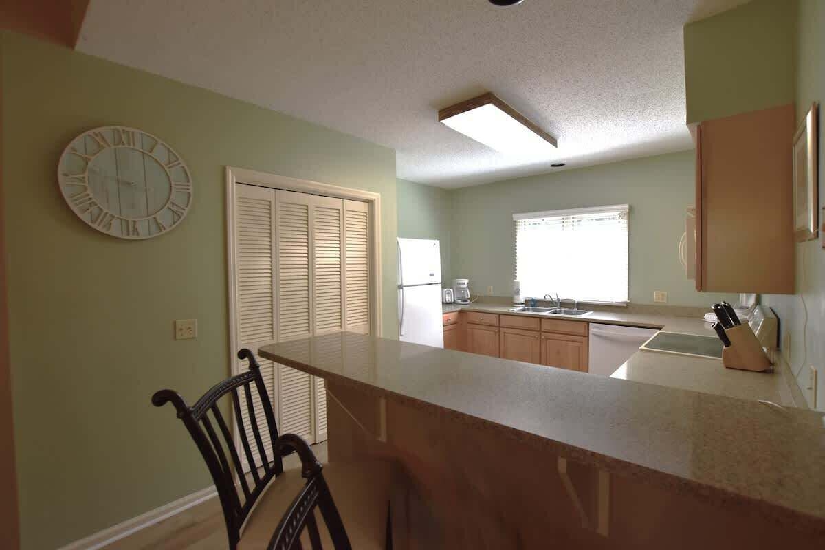 A kitchen with a bar counter, a clock, and a window with blinds.