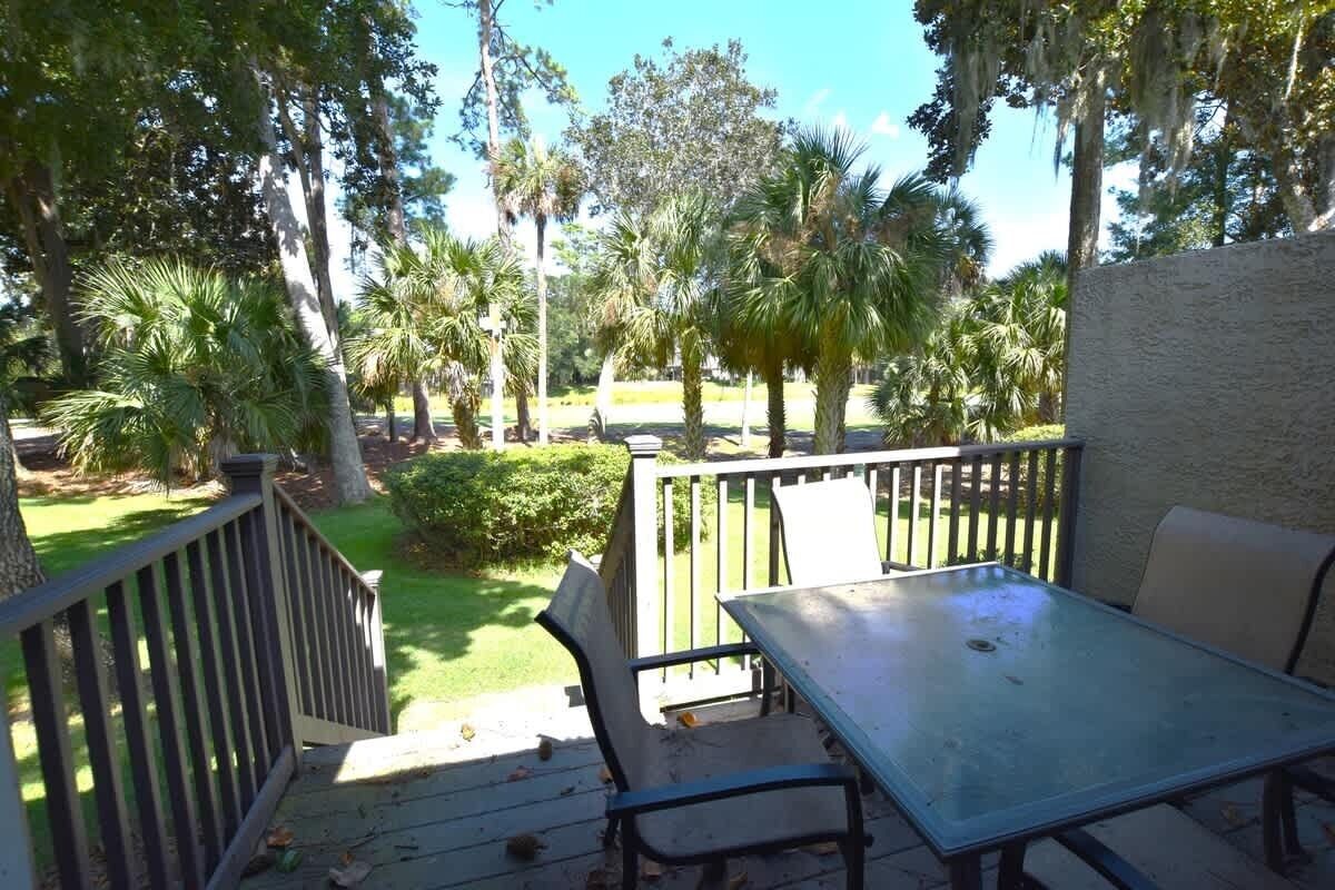 Een terras met een tafel en stoelen, omgeven door een houten hek, met uitzicht op een grasveld met bomen.