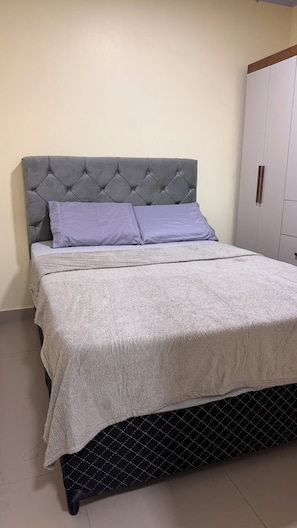 Un lit avec une tête de lit capitonnée, une couverture grise et une couette matelassée.