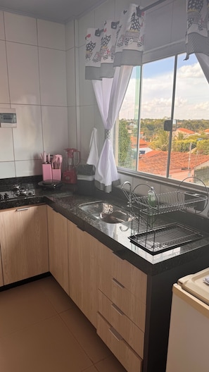 A kitchen with a large window, a sink, a stove, and wooden cabinets.