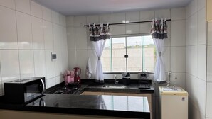 Una cocina con estufa a gas, un lavaplatos, un refrigerador y una ventana con cortinas.