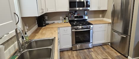 Una cocina con alacenas blancas, electrodomésticos de acero inoxidable, un lavamanos y una encimera de madera.