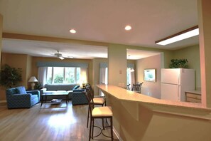 A spacious living room with a sofa, chairs, a coffee table, and a kitchen area with a refrigerator and counter. - Hilton Head Haven, Pool, Free Parking & Beach Access (Hilton Head Island)