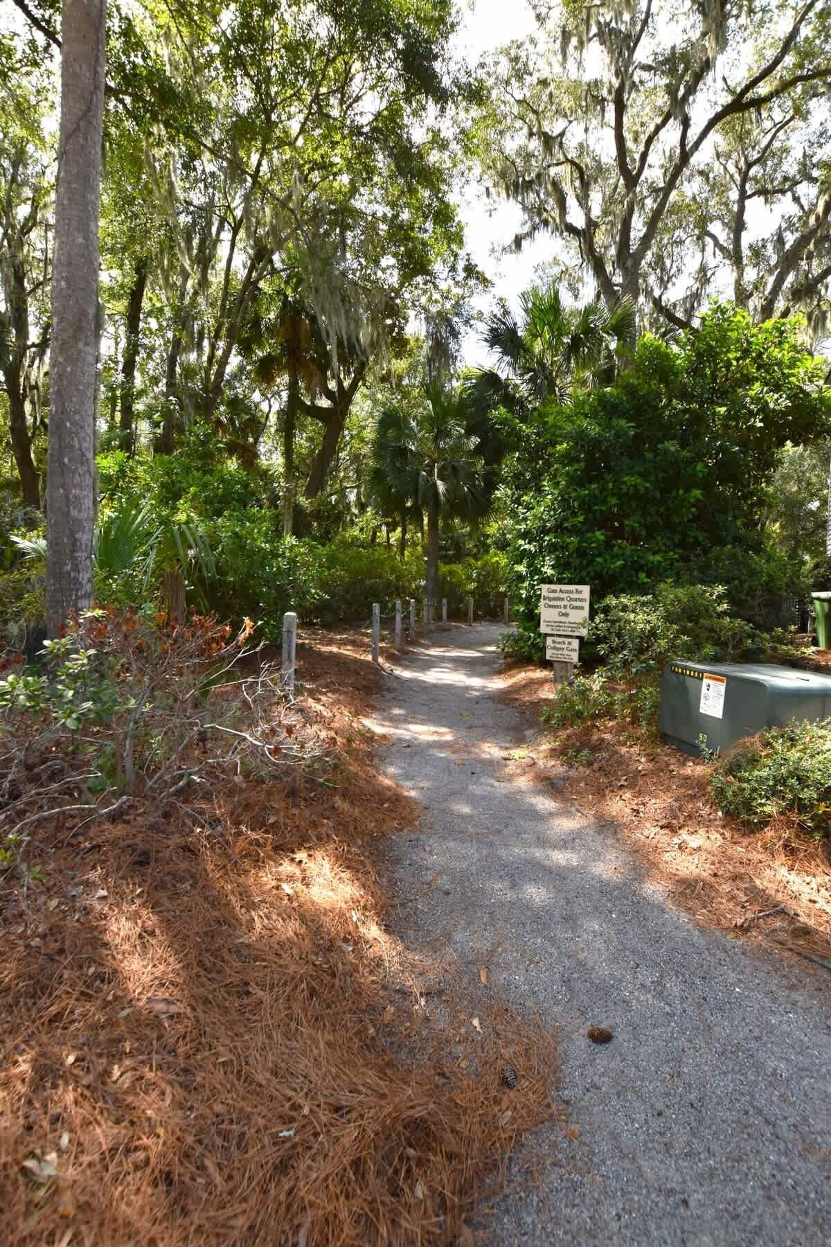 A gravel path leading through a wooded area with trees and a signpost.
