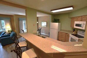 A kitchen with granite countertops, a refrigerator, microwave, stove, and a dining area with chairs. - Hilton Head Haven, Pool, Free Parking & Beach Access (Hilton Head Island)