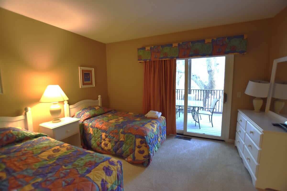 Une chambre d’hôtel avec deux lits, un balcon, une commode et une lampe.