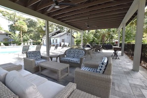 A covered outdoor seating area with wicker furniture, a pool, and a house in the background. - Hilton Head Retreat, Pool, Golf, Beach Access (Hilton Head Island)