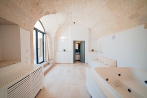 Een kamer met een stenen plafond, een groot raam, een badkuip en een deur naar een andere kamer.