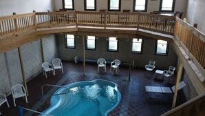 Un área de piscina interior con varios niveles, terraza de madera, múltiples zonas de estar y grandes ventanales.