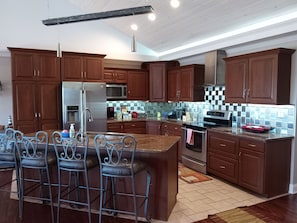 A modern kitchen with dark wooden cabinets, stainless steel appliances, and a bar area with metal stools.