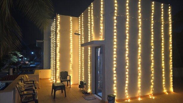 Um edifício com luzes de corda verticais, uma porta e um pequeno espaço de estar com cadeiras e uma mesa.