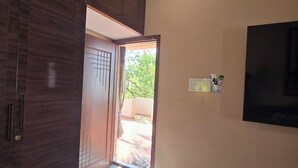Um corredor com porta de madeira escura, piso de azulejos e televisão fixada na parede.