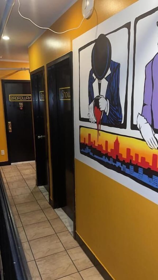 Un pasillo con puertas que dicen 'Broadway' y 'Show', un mural en la pared que representa a una persona con traje y una sustancia goteando, y un piso de baldosas.