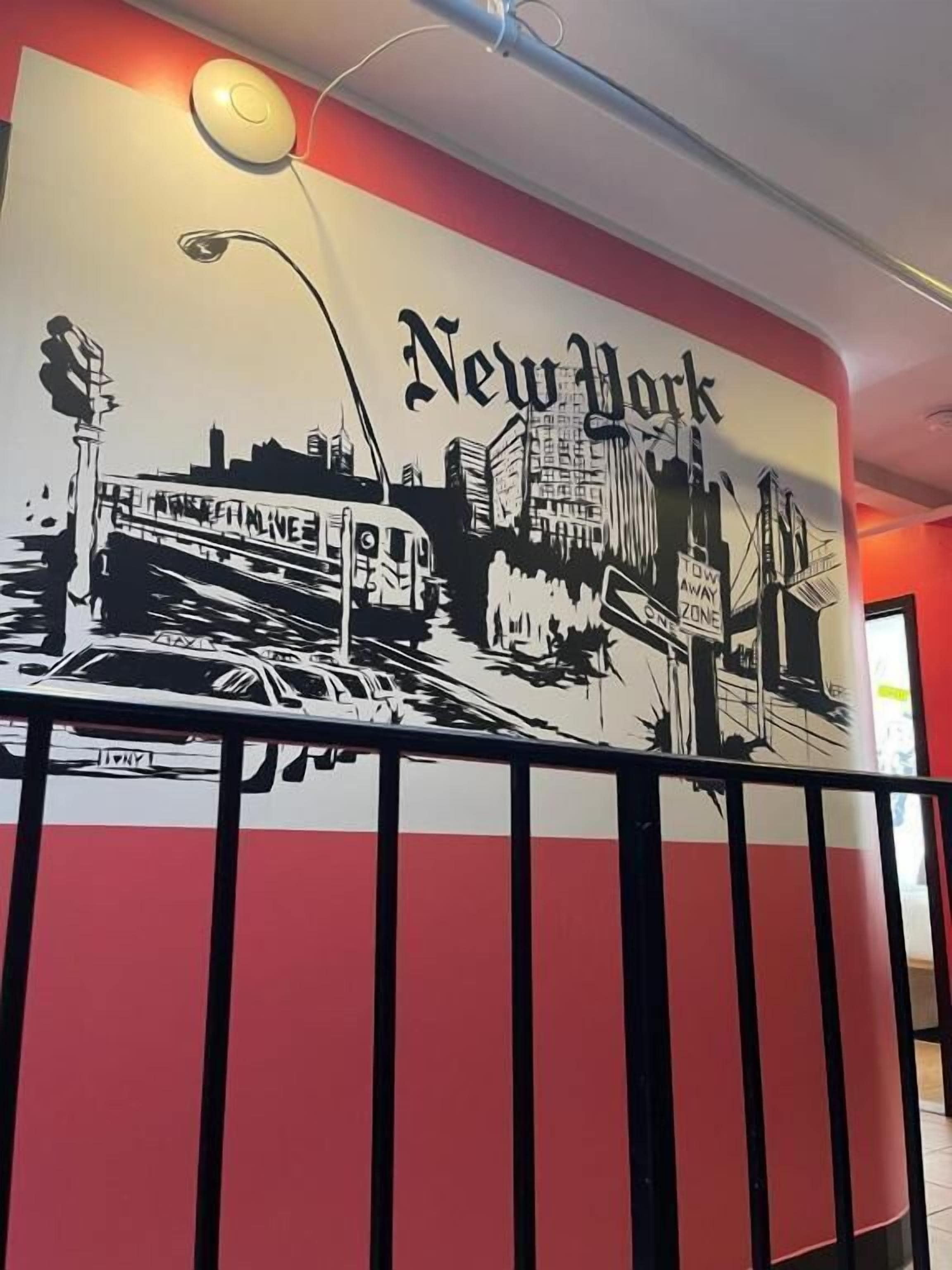 A wall mural of New York City with a subway train, buildings, and a street lamp.