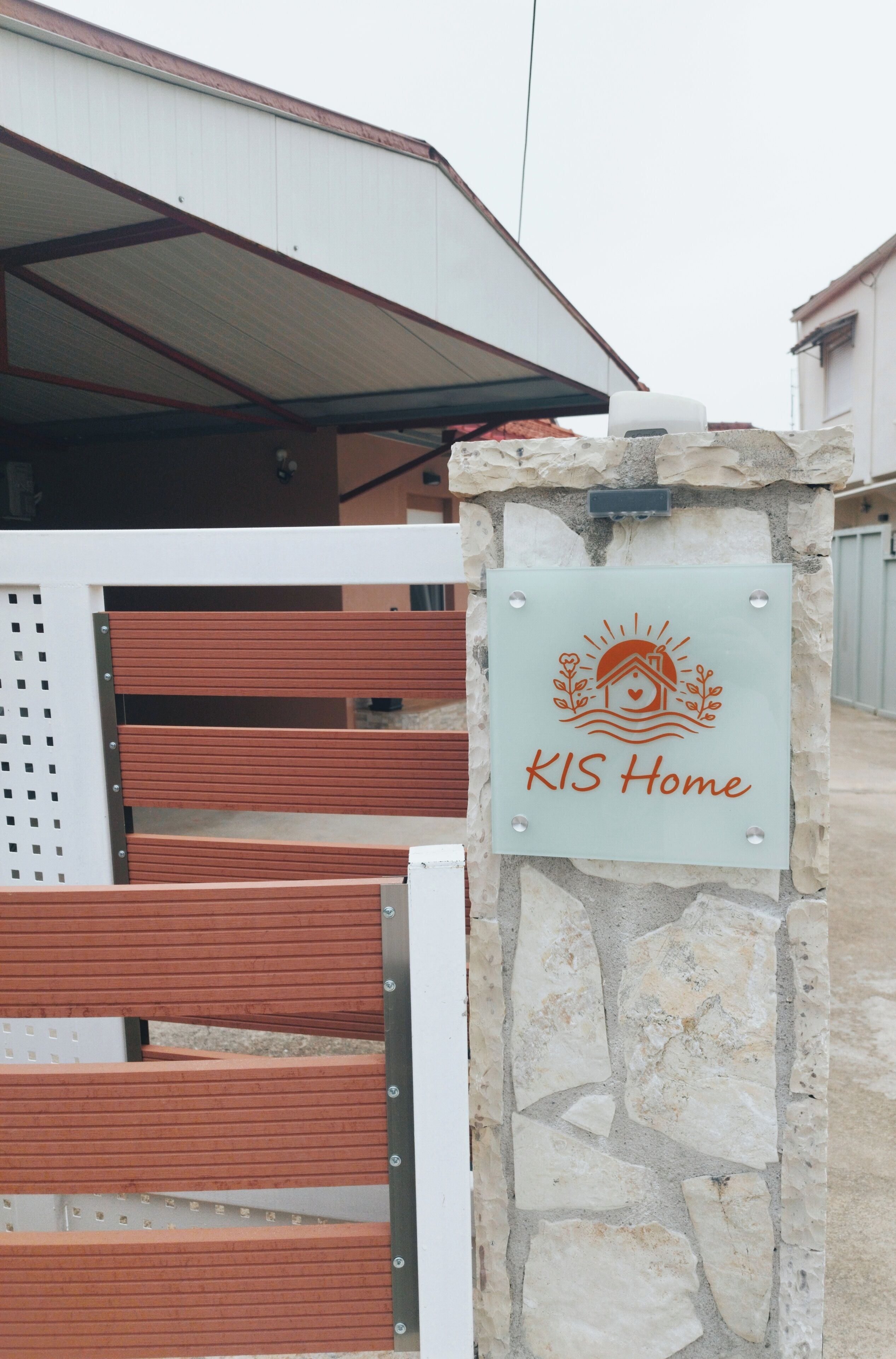 Un pilastro in pietra con un cartello che riporta 'KIS Home' e una panchina di legno.