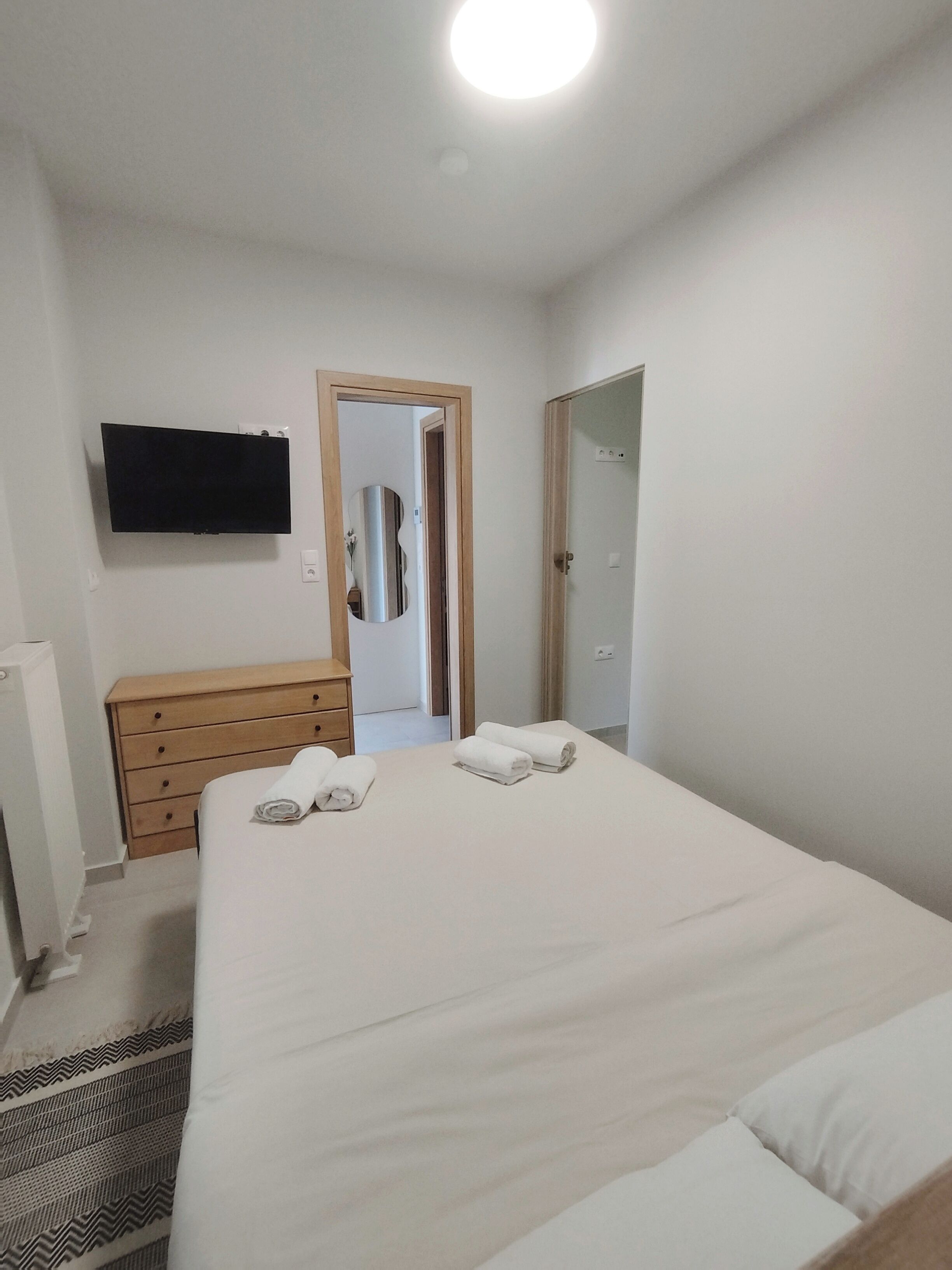 A bedroom with a bed, a dresser, a television mounted on the wall, and a door leading to another room.