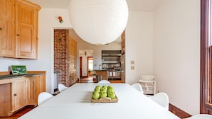 Una cocina con armarios de madera, pared de ladrillo, una mesa de comedor con manzanas y una lámpara colgante.