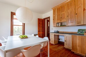 Eine moderne Küche mit Holzschränken, einem weißen Esstisch und einer Pendelleuchte.