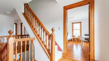 A staircase with wooden balusters leading to a room with a large window, a white radiator, and a white chair.