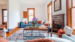 Una sala de estar con chimenea, un sofá, una mesa de centro con un jarrón de flores y una alfombra estampada.